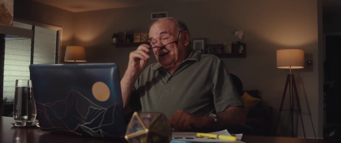 An elderly man sits at a desk looking emotional while on a video call
