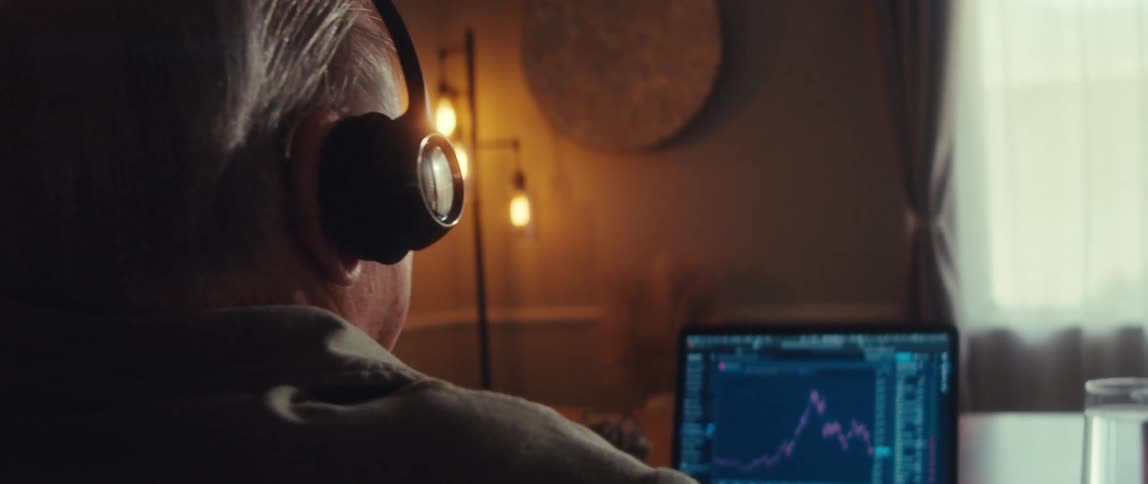 Elderly man putting on glasses trading stock market on a laptop