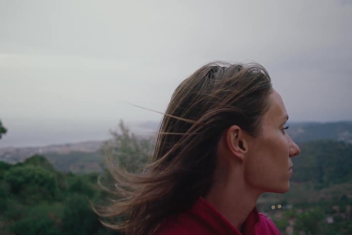 The wind is blowing the womans hair on the mountain
