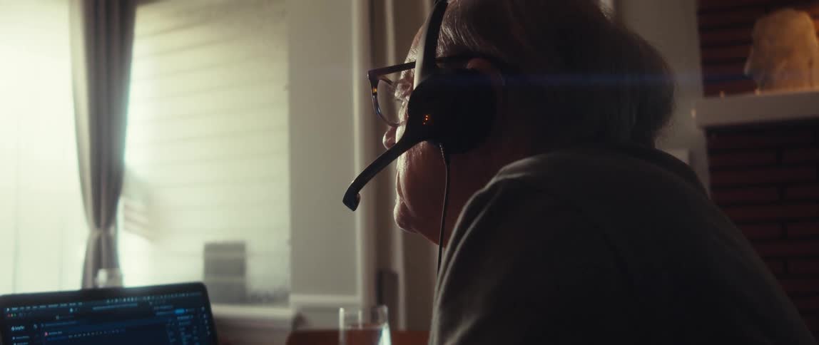 A man is pointing at the laptop and talking into his headset