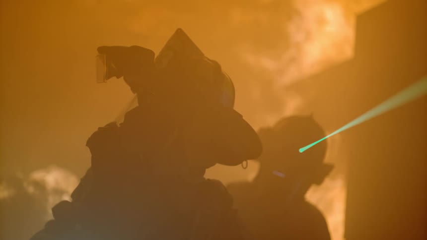 Two firefighters are outside the burning home at night