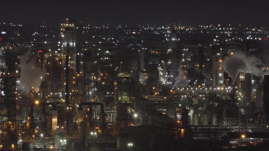 Aerial view at night of a factory dumping pollutants and a city in the background