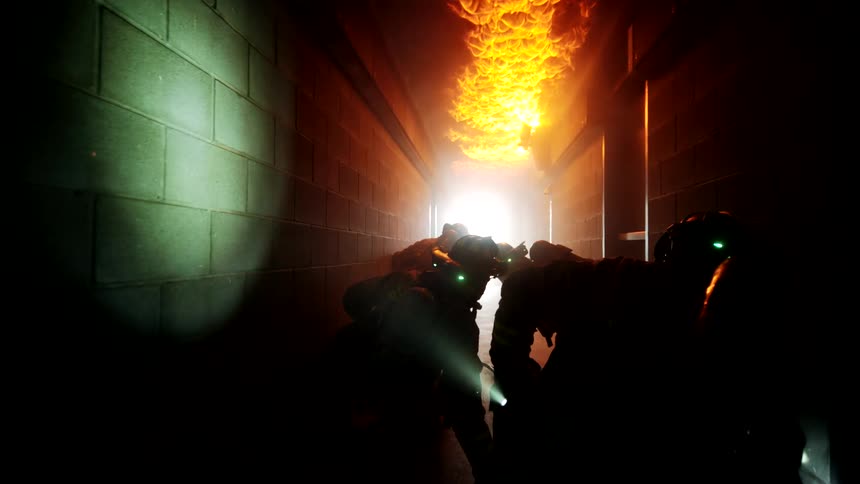 Firefighters move along a corridor with a burning ceiling on their knees