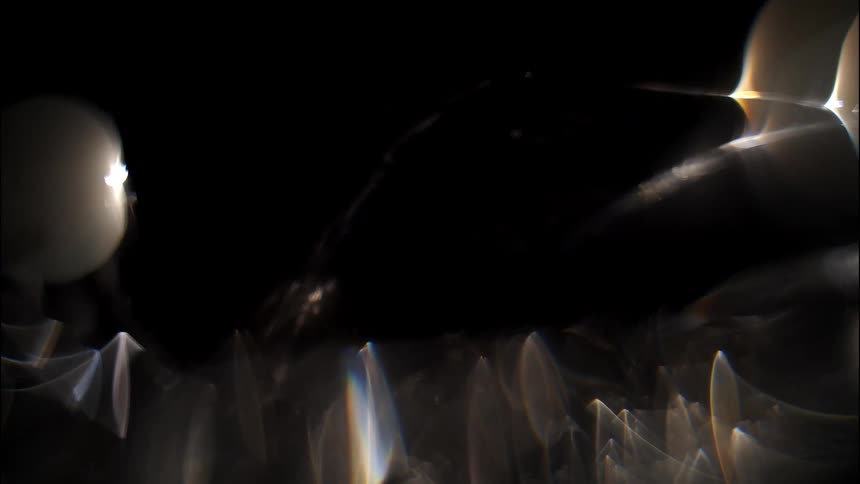 Glowing orbs and streaks of light scatter across a dark background creating layered geometric reflections
