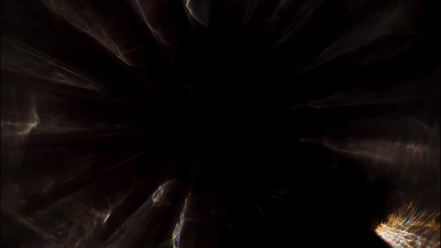 Bright lights stream outwards from the center of a dark frame creating a radial light effect