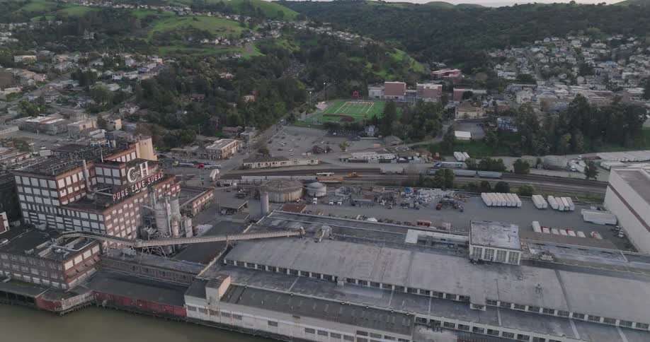 Factory on the edge of a sea canal with houses of an urban city by the mountains in the background