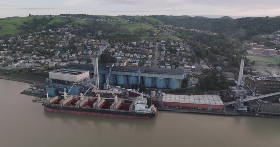 Aerial view of an industrial port with docked cargo ships beside a residential hillside town