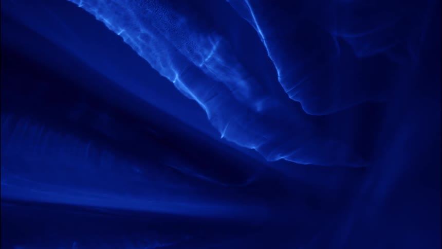 Blue streaks and light scatter across a dark backdrop forming layered geometric reflections and a luminous otherworldly glow
