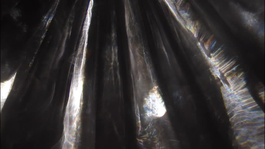 Beams of white light shimmer across a dark textured surface creating sharp reflections