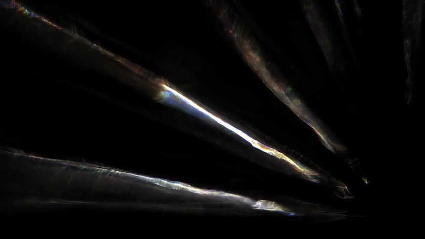 Colorful light streaks scatter across a dark background creating an abstract prismatic pattern reminiscent of reflections or refractions through glass or crystal