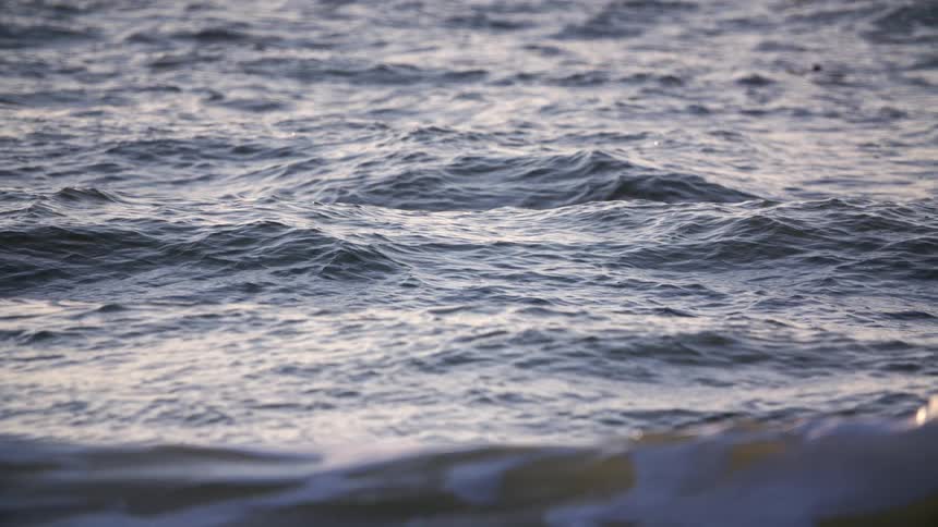 A slowmotion closeup shot captures the gentle rolling texture of dark ocean ripples and small waves on the waters surface