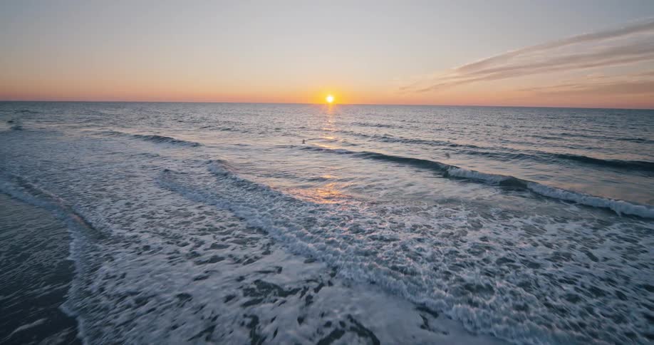 A calm ocean shoreline at sunrise with gentle waves rolling onto the beach