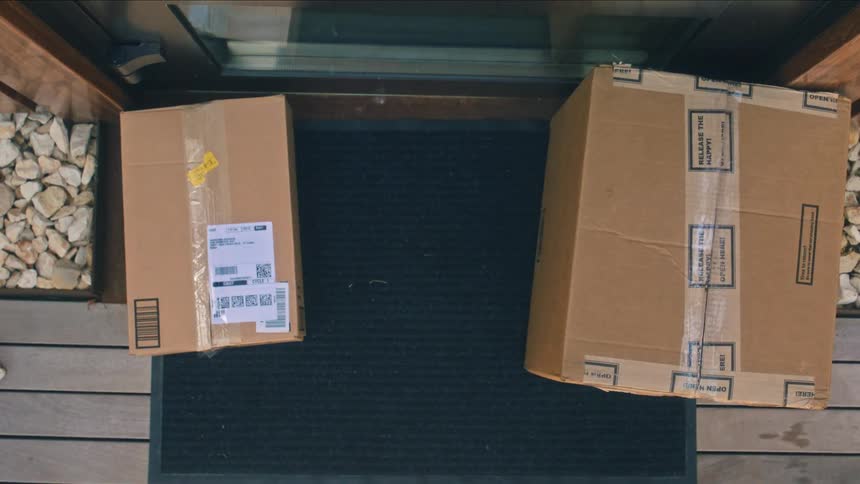 A person drops various package boxes at a doorstep during daytime