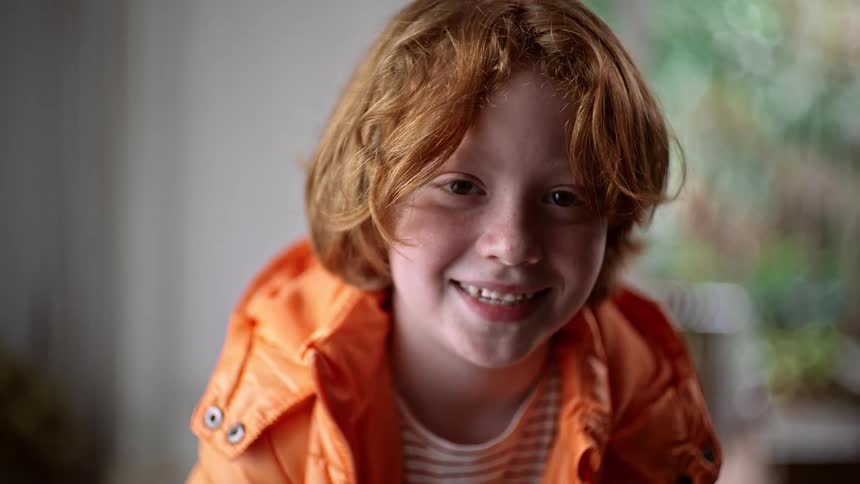 Happy red headed boy in an orange jacket smiling