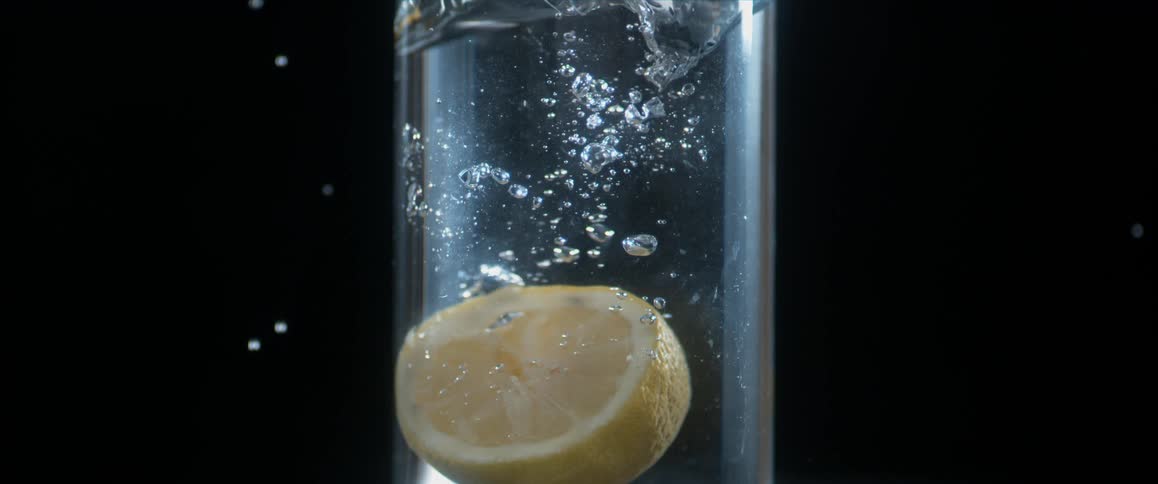 A lemon slice is dropped into a glass of water