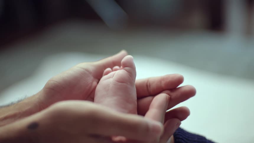 Two adult hands gently hold the foot of a baby
