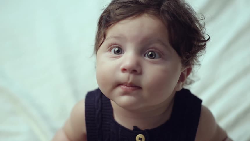 A toddler in a dark outfit looks up curiously while moving slightly
