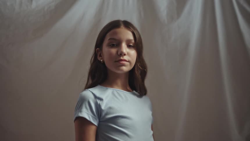Young girl in blue shirt stands confidently against fabric backdrop