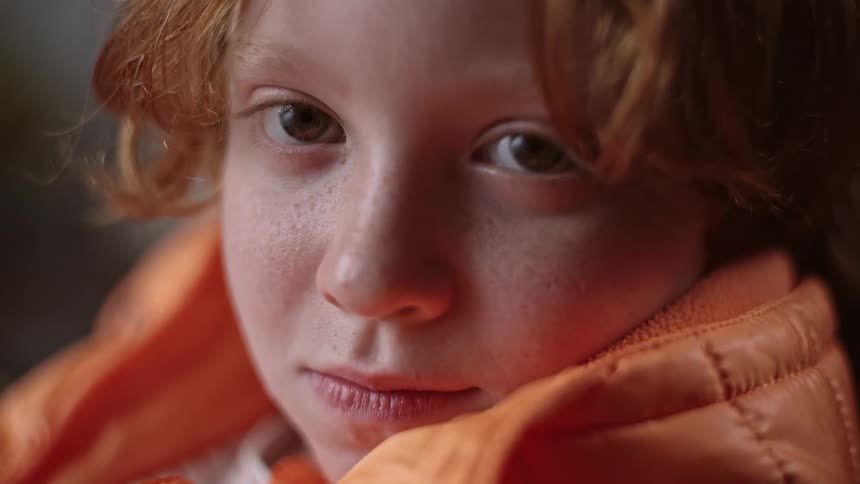 A boy earing an orange jacket smiles
