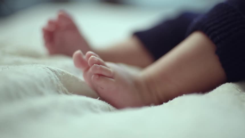 Close up of a baby wriggling their feet while lying on a bed