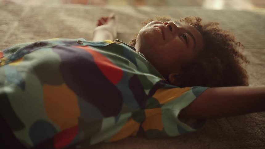 A little boy sprawls out on his bed while smiling and nodding his head