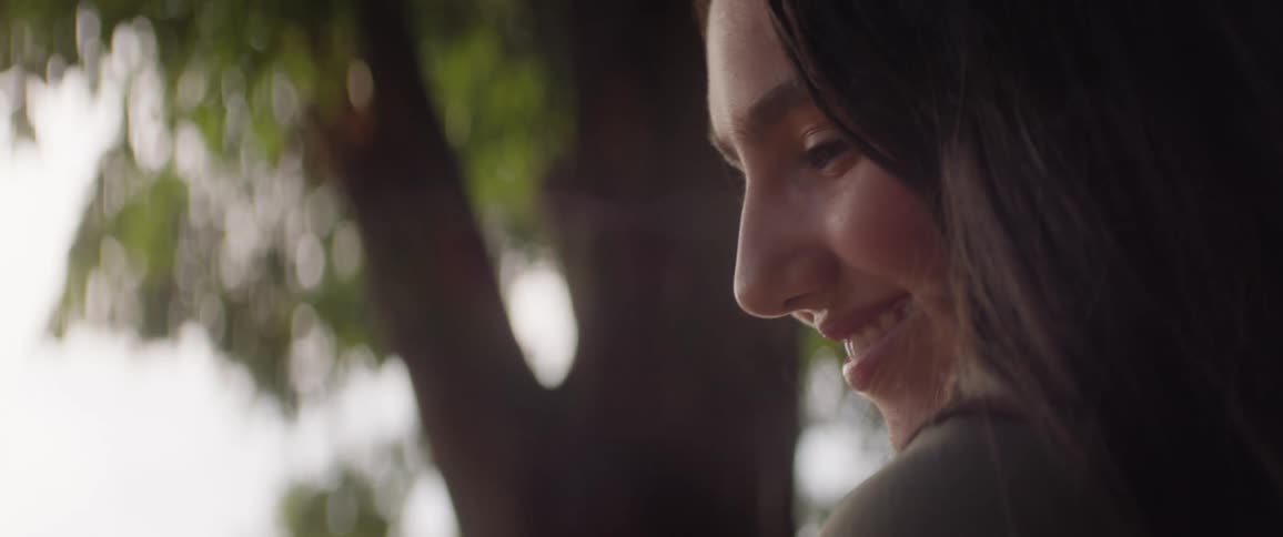 The face of a teenage girl who has a subtle smile on her face next to a tree she she she is looking to her left side