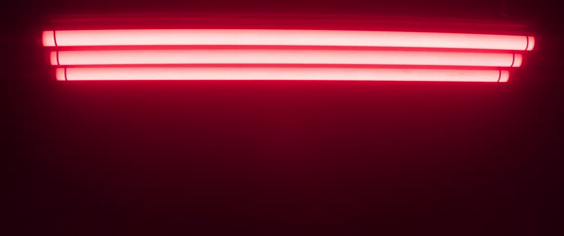 Several long glowing red tube lights are mounted horizontally and suspended against a dark background