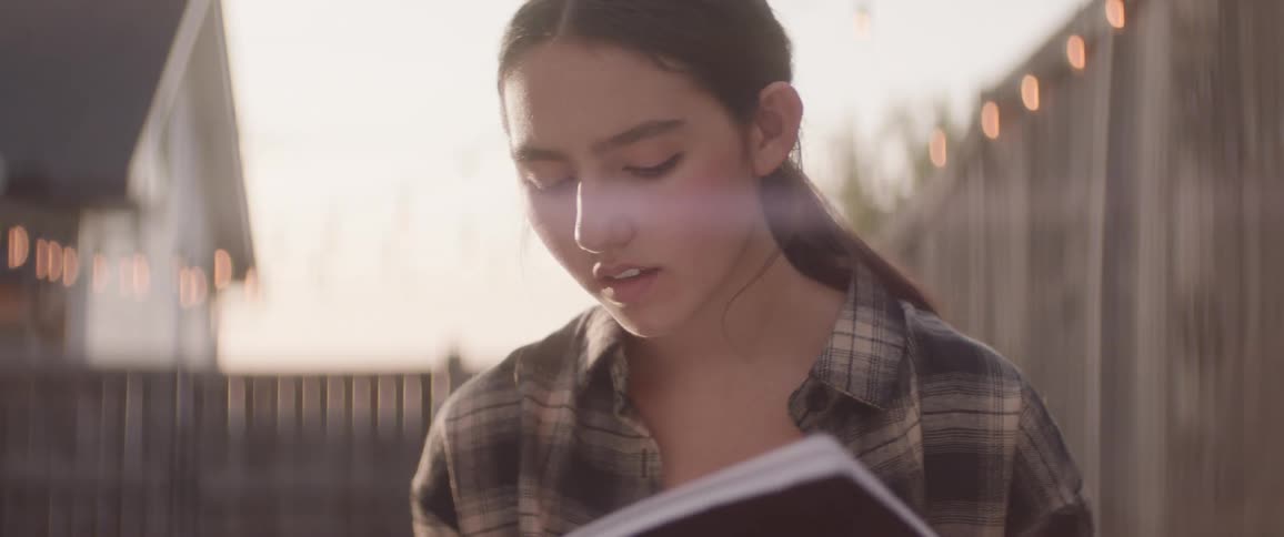 The face of a teenage girl who is in an outdoor moment and is holding a white paper and reading it