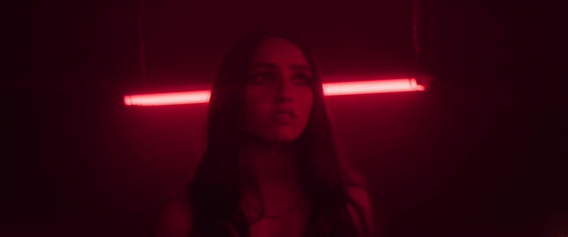 Frightened woman slowly looks around room lit by a dim red fluorescent light