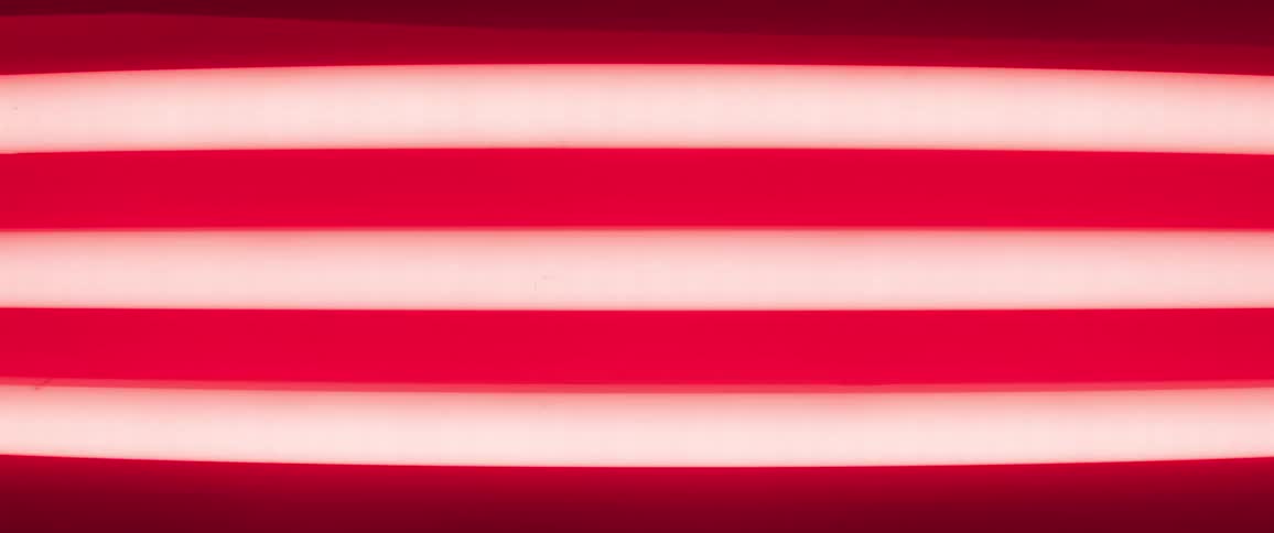 Three fluorescent light tubes cast red light on the ceiling