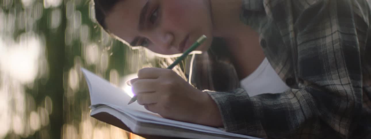 The face of a teenage girl who is using a green pencil to write on me a book with a white paper