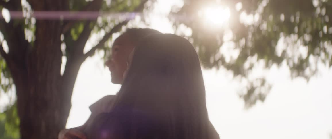Mother holding her daughter in her arms while standing under a tree