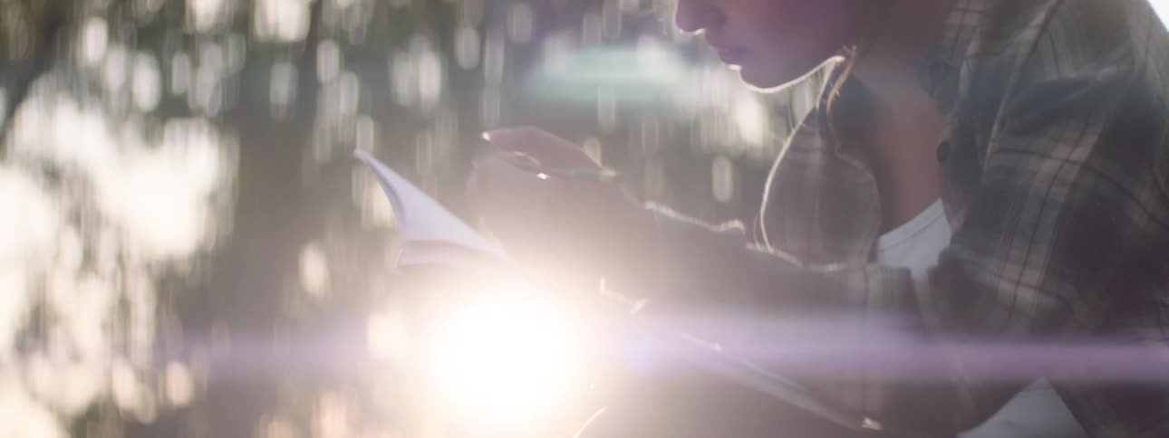 Close up of a female teenager sketching with a pencil in a sketchbook while sitting outdoors during daytime