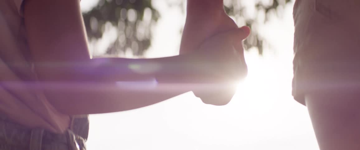 Two people holding hands in an outdoor setting with sunlight reflecting