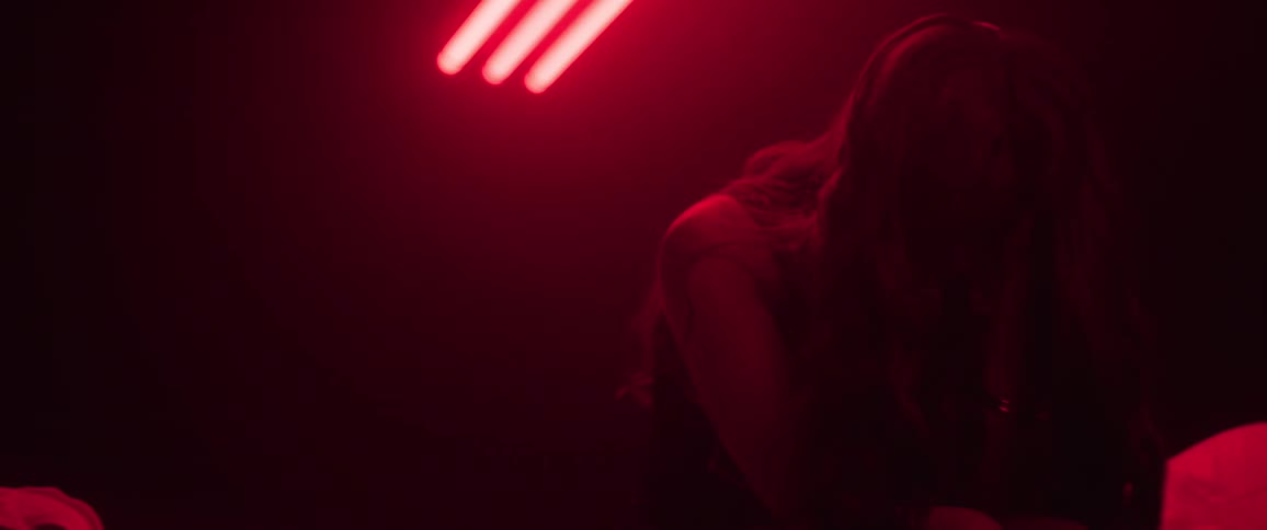 Woman sitting with a bowed head in aroom lit by red light raises her head