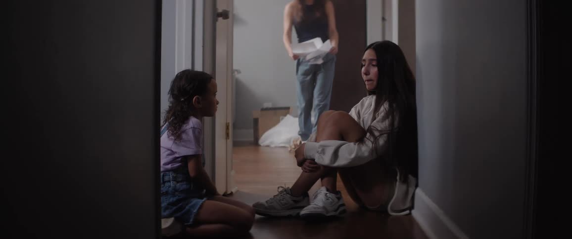 Two girls sit on the floor while another woman looks at papers in frustration