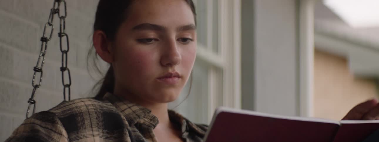 The face of a teenage girl who is on a swing holding a pen and looking at a book