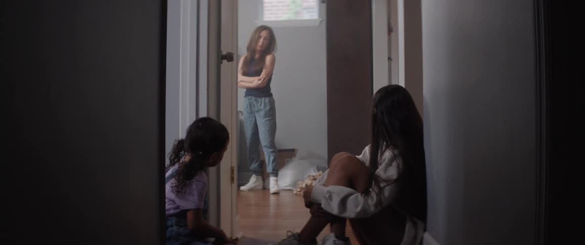 A mother shakes her head in disappointment at her two daughters sitting on the hallway floor