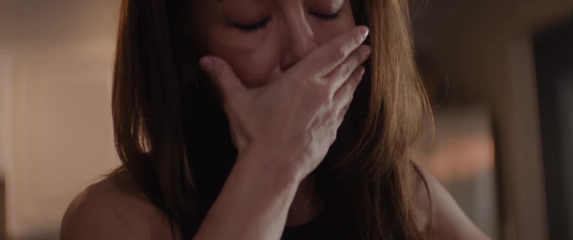 A woman covers her mouth with her hand and looks downward with a sad expression
