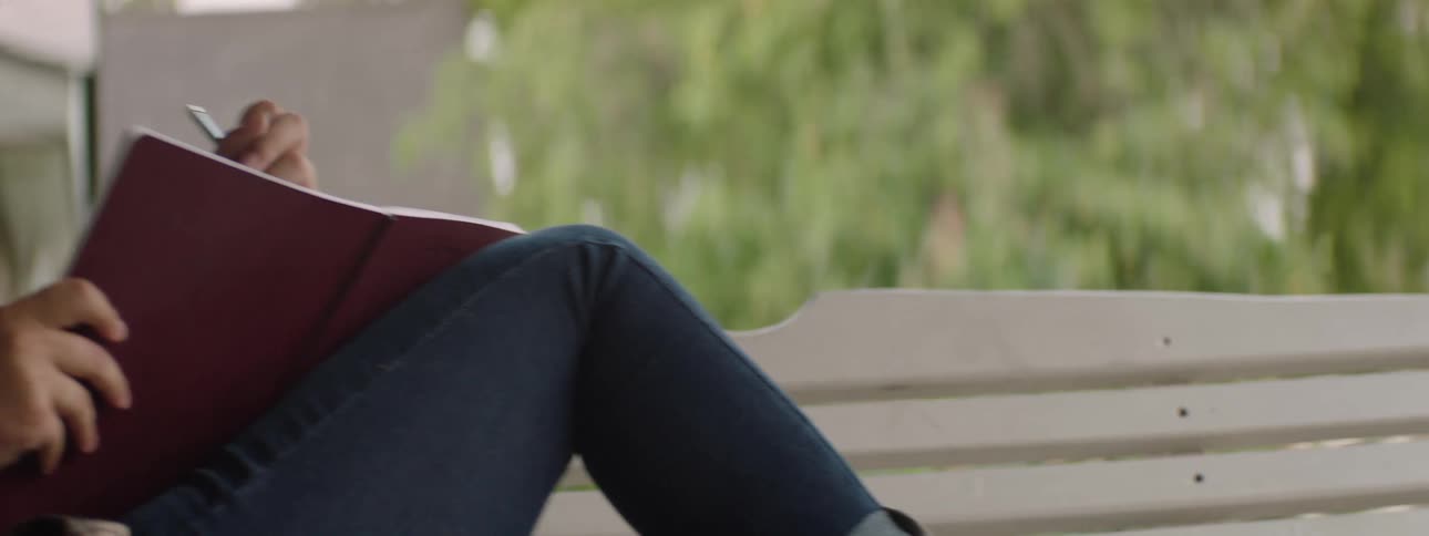A girl sits on a porch swing thoughtfully writing in a notebook