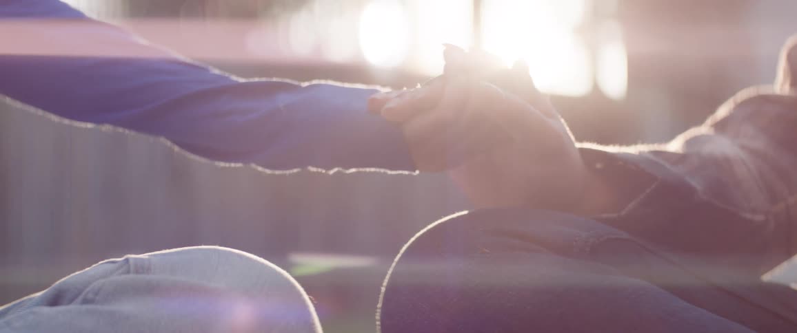 Two people sit closely together and gently hold hands in a quiet intimate moment