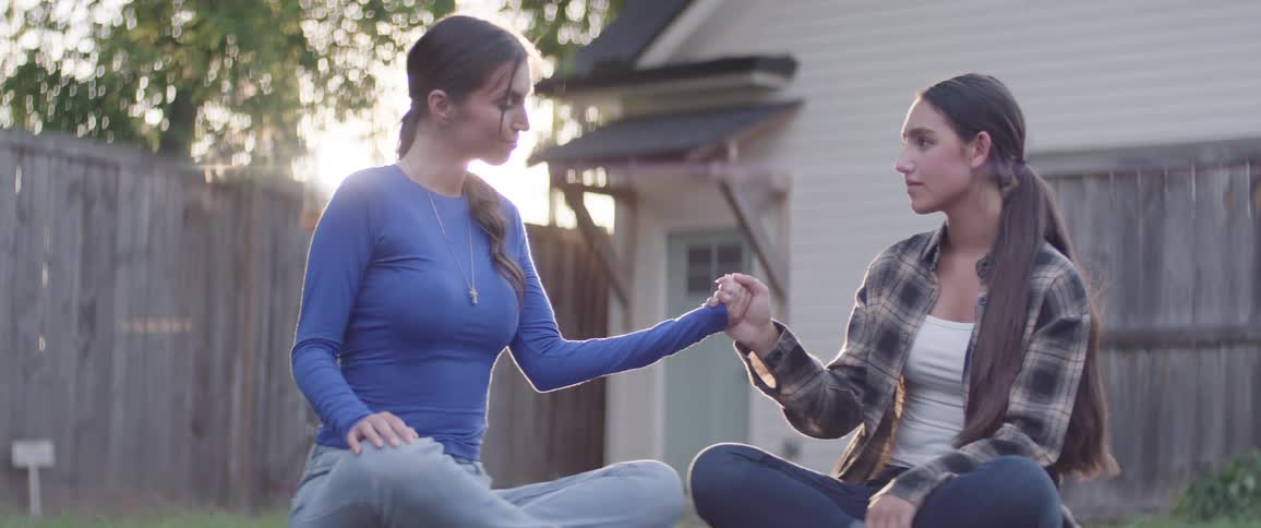 Young women hold hands while sitting in the yard and meditating