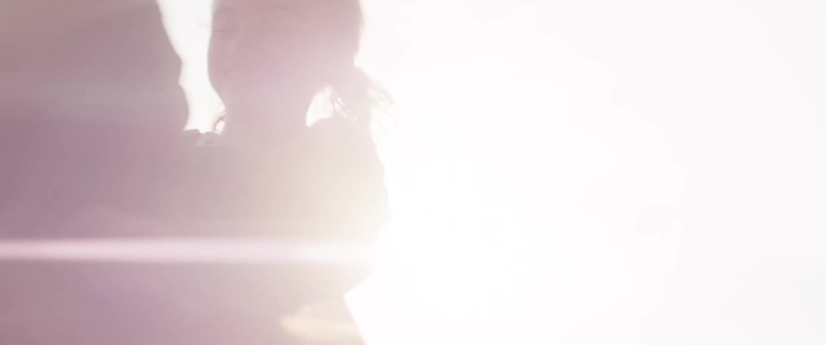 A person and a young child are silhouetted against a bright hazy sky looking at each other with a strong sun flare between them