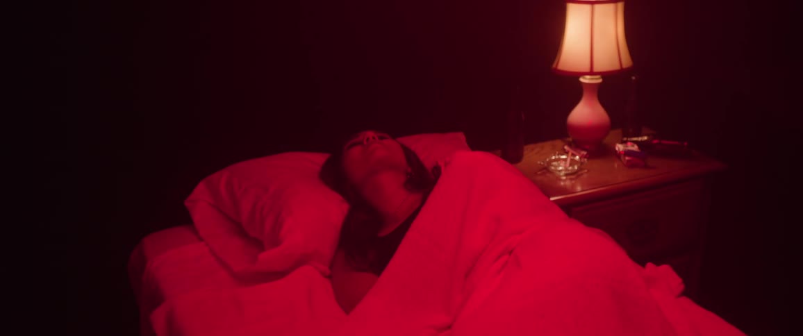 Woman lying on a bed in a bedroom lit by red lighting pulls the covers over her head