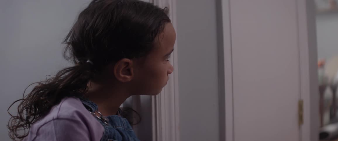 The face of a little girl wearing a purple outfit and she is looking at a white door in sad tones