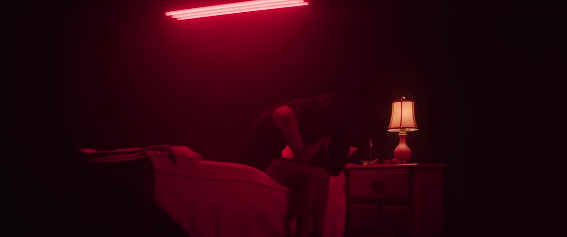 Woman sitting on a bed with her head in her hands in a dimly lit room