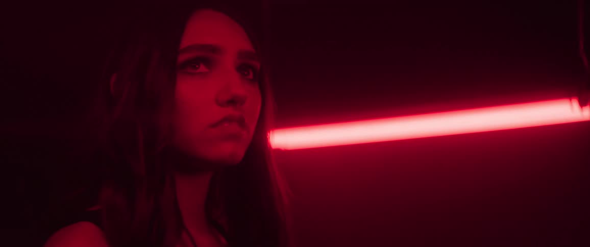 Woman looks around at the ceiling while in a room lit by red fluorescent lights