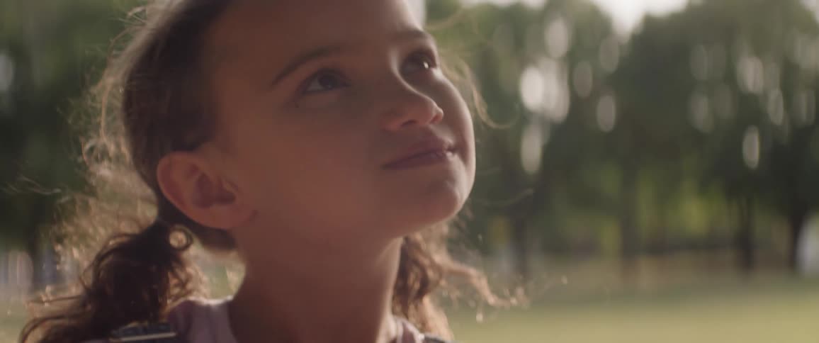 A child with brown hair looks upwards and smiles with a light colored background