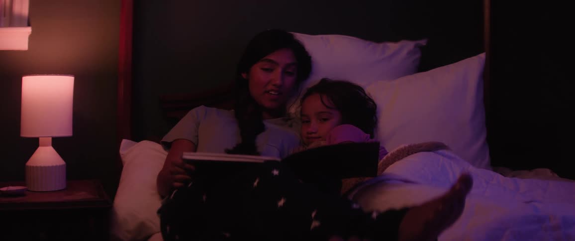 Female teenager reads a book to her younger sister in bed at night before bedtime
