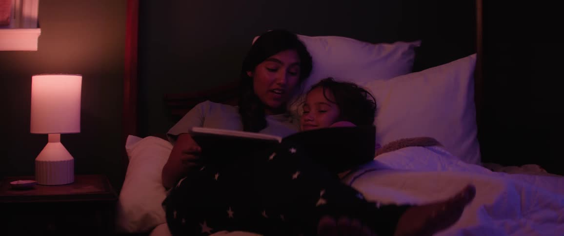 Female teen reads a book to her younger sister in bed at night before bedtime